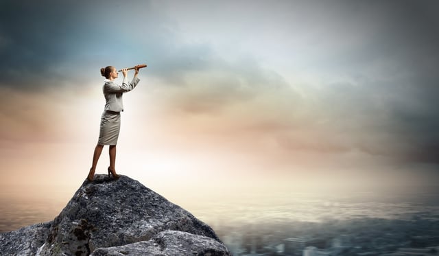 Businesswoman looking in telescope standing atop of rock